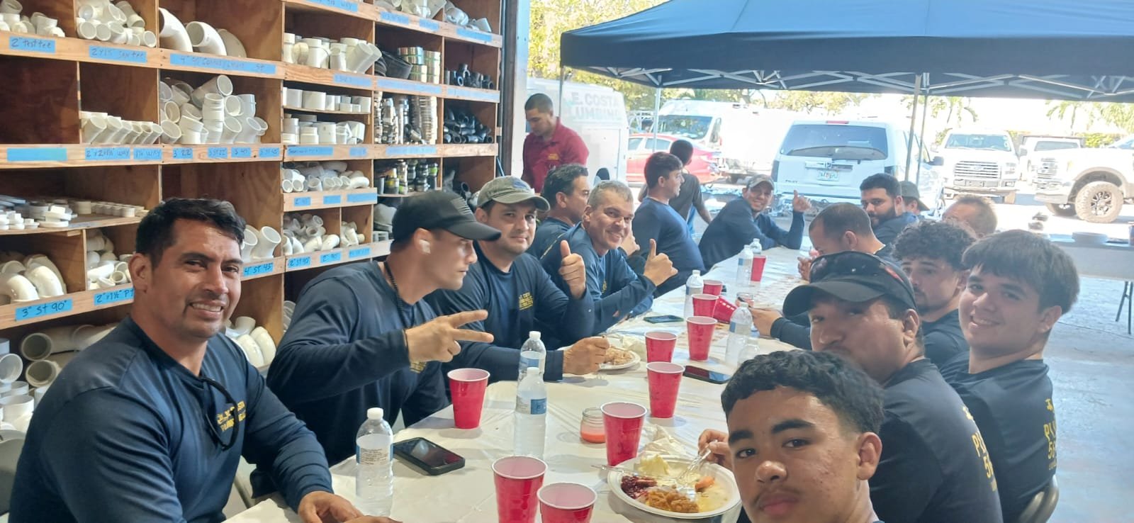Team lunch at the E. Costa Plumbing warehouse in West Palm Beach, surrounded by shelves of fittings